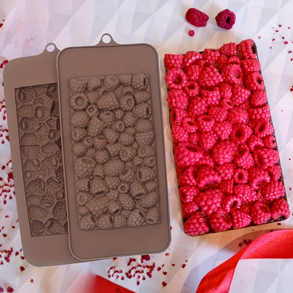 A silicone mold set shown next to a rectangular sample of raspberry-patterned material, with two loose raspberries on a white patterned surface.